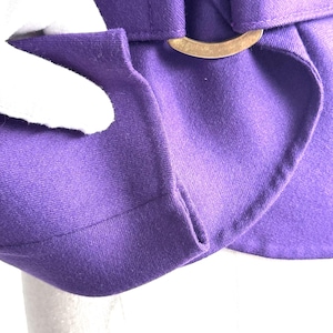 Pode incluir: Close-up de uma pe&ccedil;a de roupa roxa vibrante com um design estruturado. O tecido &eacute; de cor s&oacute;lida e a pe&ccedil;a de roupa apresenta uma fivela dourada e uma presilha. A textura do tecido &eacute; vis&iacute;vel.