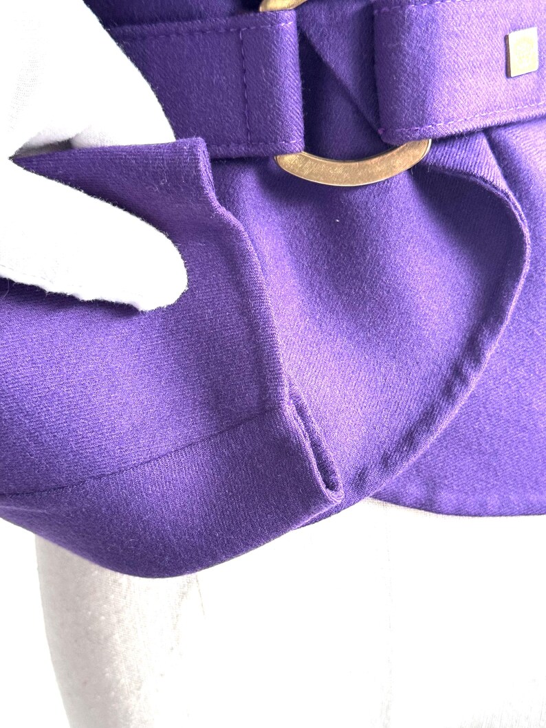 Pode incluir: Close-up de uma pe&ccedil;a de roupa roxa vibrante com um design estruturado. O tecido &eacute; de cor s&oacute;lida e a pe&ccedil;a de roupa apresenta uma fivela dourada e uma presilha. A textura do tecido &eacute; vis&iacute;vel.