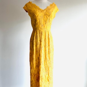 May include: A vintage yellow dress with a V-neckline and cap sleeves. The dress features intricate floral embroidery and a fitted bodice that flows into a knee-length skirt. The dress is displayed on a mannequin.