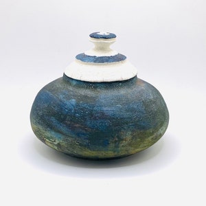 May include: A ceramic jar with a lid, featuring a blue and green glaze with white accents. The jar has a rounded shape and a smooth, textured surface.