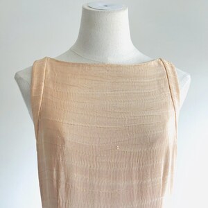 May include: A sleeveless, peach-colored dress with a textured, ribbed fabric. The dress has a boat neckline and is displayed on a mannequin. The fabric has a subtle, horizontal wave pattern.