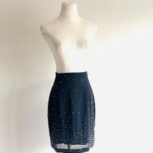 May include: A black knee-length skirt featuring a high-waisted design and a dense scattering of small, reflective silver-toned beads that increase in concentration toward the bottom hem, creating a gradient effect on the solid black fabric.