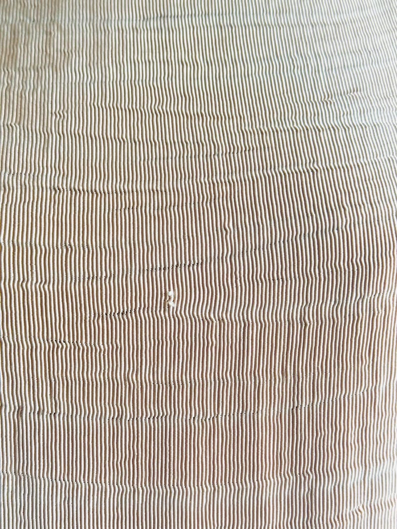 May include: Close-up of a fabric with a vertical striped pattern. The stripes alternate between a light beige and a darker brown color. The fabric has a slightly textured appearance, with subtle variations in the stripes.