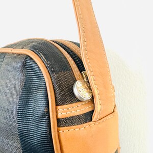 May include: A brown leather shoulder strap with a black and brown patterned bag. The bag has a zipper closure and a gold metal button with the letter "F" on it.