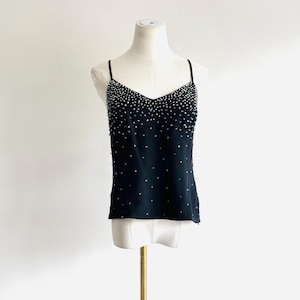 May include: A black camisole top featuring a V-neckline and thin spaghetti straps. The front of the garment is embellished with numerous small, reflective silver-toned beads that are densely concentrated at the top and sparse toward the hem.