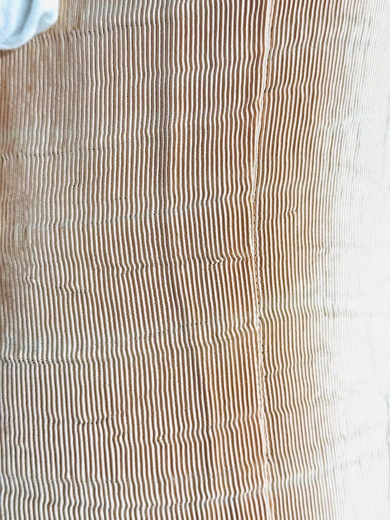 May include: Close-up of a textured fabric with vertical stripes. The stripes transition from a warm brown to a white color, creating a gradient effect. The fabric appears to be soft and possibly quilted.