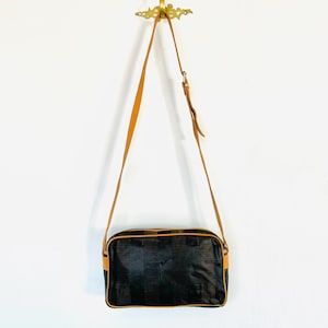 May include: A brown leather shoulder bag with a black and brown patterned fabric body. The bag has a rectangular shape and a single strap.