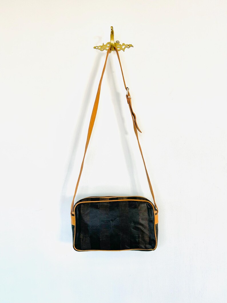 May include: A brown leather shoulder bag with a black and brown patterned fabric body. The bag has a rectangular shape and a single strap.