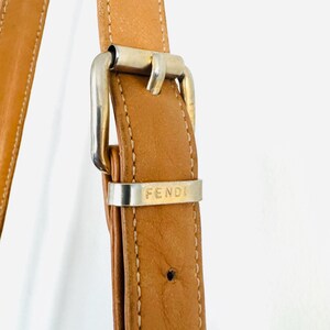 May include: Close-up of a brown leather shoulder strap with a silver buckle. The buckle has the word "FENDI" engraved on it.