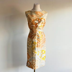 Könnte beinhalten: Ein ärmelloses Vintage-Kleid mit einem lebendigen Muster in Orange, Gelb und Creme. Das Kleid, das auf einer Schaufensterpuppe präsentiert wird, hat ein figurbetontes Oberteil und einen knielangen Rock. Der Stoff zeigt ein wellenartiges Muster.