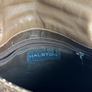 K&ouml;nnte beinhalten: Eine braune Lederhandtasche mit Schlangenmuster. Der Innenraum hat ein dunkelbraunes Futter und einen Rei&szlig;verschluss. Das Etikett "HALSTON" ist im Inneren der Tasche sichtbar.