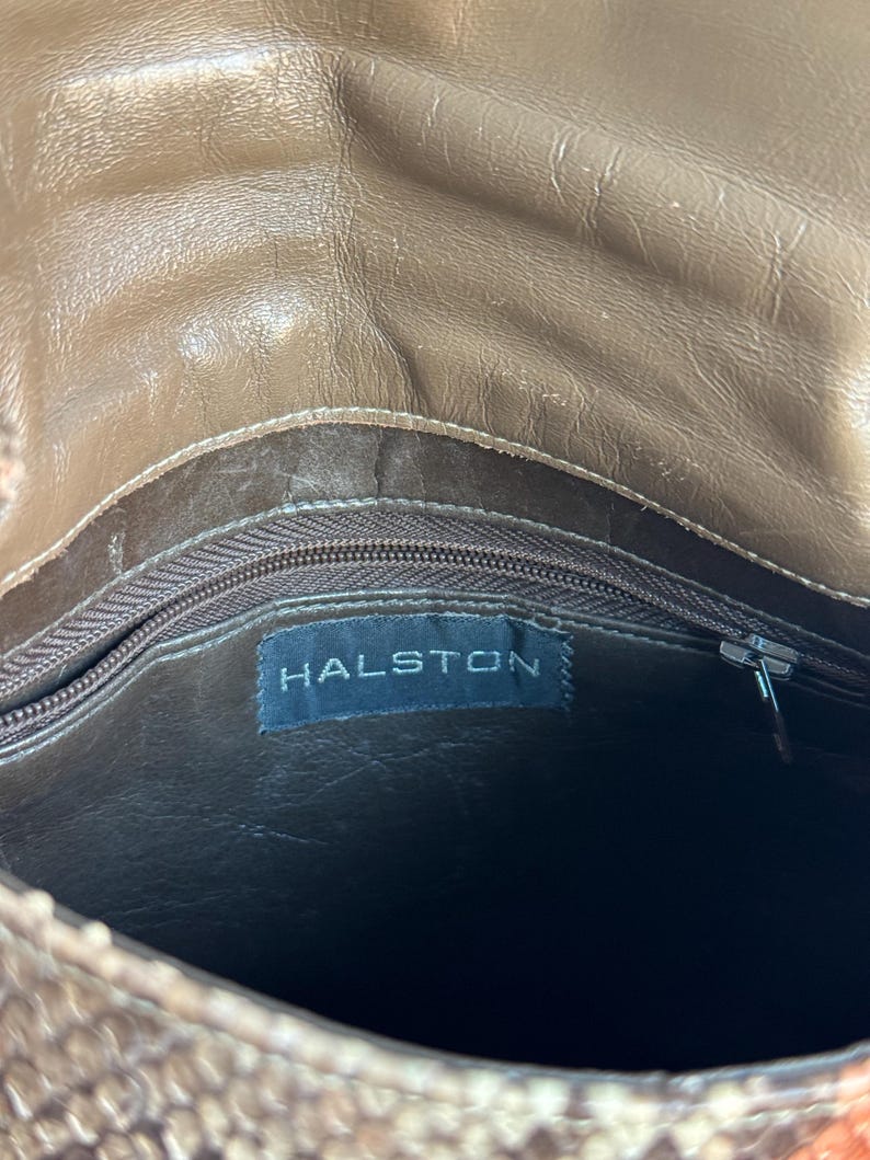 K&ouml;nnte beinhalten: Eine braune Lederhandtasche mit Schlangenmuster. Der Innenraum hat ein dunkelbraunes Futter und einen Rei&szlig;verschluss. Das Etikett "HALSTON" ist im Inneren der Tasche sichtbar.