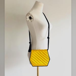 May include: A vintage yellow Valentino crossbody bag with a black trim and strap. The bag has a textured, pleated design and a black tassel. The text "80s Valentino" is visible.
