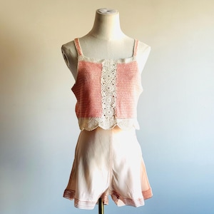 May include: A peach-colored crochet top with a cream-colored lace panel and straps, paired with matching peach shorts. The shorts have a scalloped hem with a striped border. The outfit is displayed on a mannequin.
