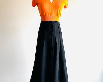 Può includere: Una gonna midi nera con chiusura a bottoni e vita aderente. La gonna è abbinata a un maglione arancione a maniche corte con scollo a chiave.