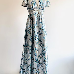 May include: A long, flowing silver and blue paisley patterned dress with a V-neckline and short sleeves. The dress has a tie at the waist.