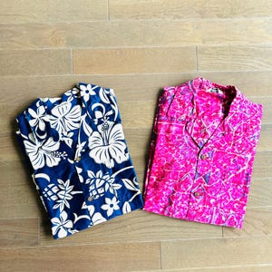 Könnte beinhalten: Zwei Hawaiihemden, eines blau mit weißem Blumendruck und eines pink mit mehrfarbigem Blumendruck.