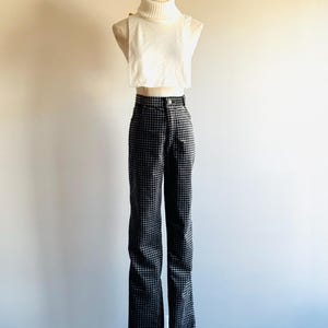 Könnte beinhalten: Ein cremefarbenes Rollkragen-Crop-Top und eine hoch taillierte, schwarz-weiß karierte Hose werden auf einer Schaufensterpuppe präsentiert. Die Hose hat ein ausgestelltes Bein. Das Outfit steht vor einer schlichten, hellen Wand.