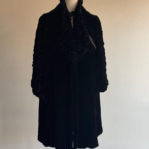 K&ouml;nnte beinhalten: Eine schwarze Samtjacke mit einem R&uuml;schenkragen und langen &Auml;rmeln. Die Jacke befindet sich auf einem Mannequin.
