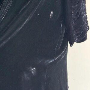 K&ouml;nnte beinhalten: Eine schwarze Samtjacke mit R&uuml;schenkragen und leicht gerafftem &Auml;rmel. Die Jacke hat ein paar helle Flecken auf dem Stoff.