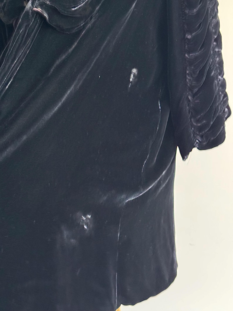 K&ouml;nnte beinhalten: Eine schwarze Samtjacke mit R&uuml;schenkragen und leicht gerafftem &Auml;rmel. Die Jacke hat ein paar helle Flecken auf dem Stoff.