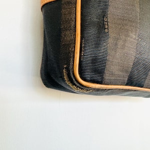 May include: A brown and black striped fabric handbag with a brown leather trim. The bag has a brown leather strap and the brand name "FENDI" is visible on the fabric.