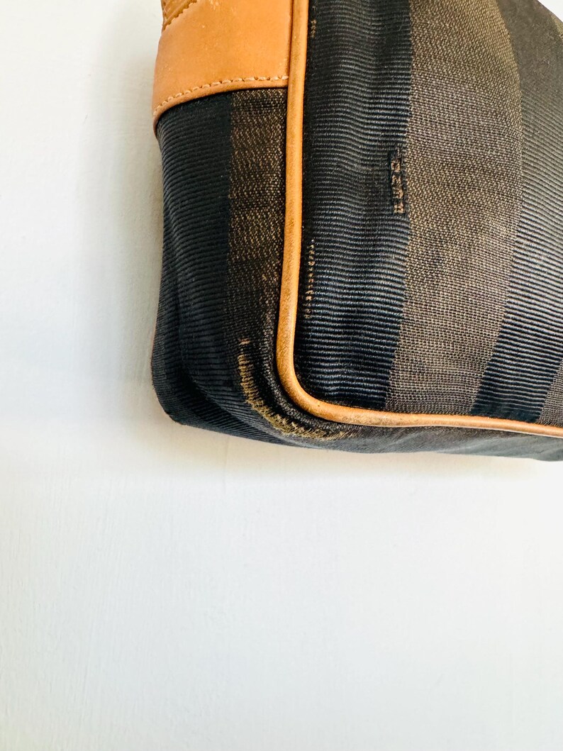 May include: A brown and black striped fabric handbag with a brown leather trim. The bag has a brown leather strap and the brand name "FENDI" is visible on the fabric.