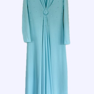 Könnte beinhalten: Ein hellblaues, langärmliges Kleid mit V-Ausschnitt und einem Knotendetail am Halsausschnitt. Das Kleid ist mit kleinen, glitzernden Verzierungen verziert.