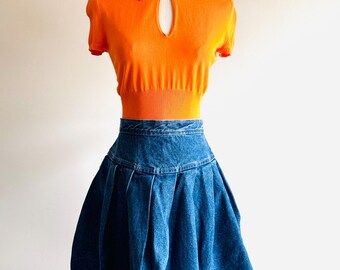 Può includere: Un top arancione brillante a maniche corte con colletto e un'apertura a forma di buco della serratura sul davanti, abbinato a una gonna di jeans blu plissettata.