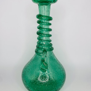 May include: A green glass vase with a textured surface and a spiral design around the neck. The vase has a bulbous base.