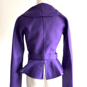 Pode incluir: Uma jaqueta roxa vibrante com gola larga e cintura com cinto. A jaqueta apresenta mangas compridas e bainha estilo peplum. A parte de tr&aacute;s da jaqueta &eacute; vis&iacute;vel, mostrando seu design sob medida e um detalhe de fenda na parte inferior.