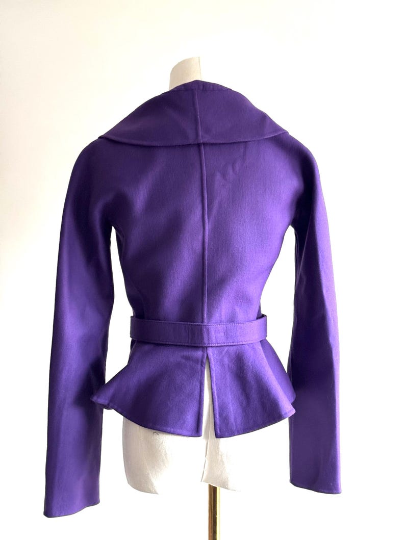Pode incluir: Uma jaqueta roxa vibrante com gola larga e cintura com cinto. A jaqueta apresenta mangas compridas e bainha estilo peplum. A parte de tr&aacute;s da jaqueta &eacute; vis&iacute;vel, mostrando seu design sob medida e um detalhe de fenda na parte inferior.