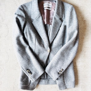 May include: A gray wool blazer with a single-button closure and three buttons on each sleeve. The blazer has a notched lapel and a satin lining. The label inside the blazer reads "Yves Saint Laurent".