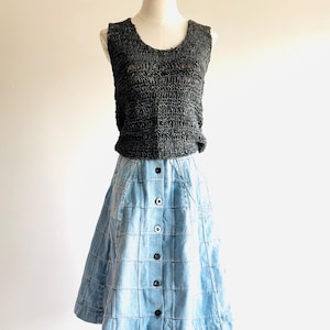 May include: A sleeveless charcoal top and a light blue denim skirt on a mannequin. The top has a textured, woven appearance. The skirt features a grid pattern and a button-down front. The outfit is displayed against a neutral background.