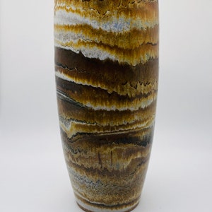 May include: A tall, cylindrical ceramic vase with a brown, white, and black striped pattern. The vase has a smooth, glazed finish.