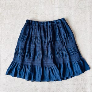 May include: A navy blue skirt with a tiered design. The skirt has a gathered waistband and a flared hem. The fabric appears to be a lightweight material, suitable for warm weather. The skirt is displayed on a neutral background.