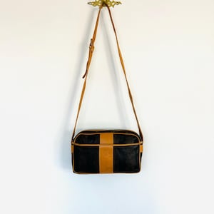 May include: A black and brown leather shoulder bag with a long strap. The bag has a brown leather trim and a small logo on the front.