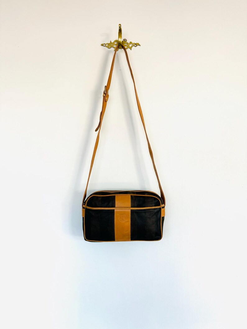 May include: A black and brown leather shoulder bag with a long strap. The bag has a brown leather trim and a small logo on the front.
