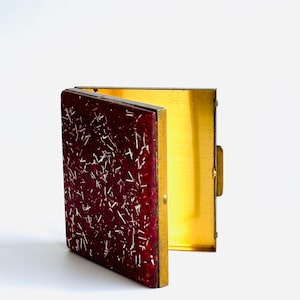 May include: A vintage red and gold cigarette case with a white speckled design. The case is open and the inside is gold.