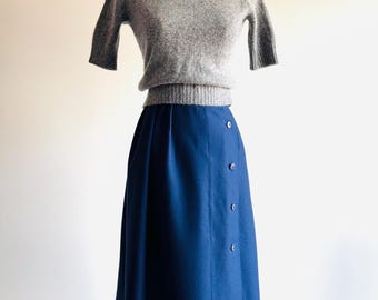 May include: A gray turtleneck sweater with short sleeves and a navy blue skirt with a button closure. The skirt is knee-length and has a slight A-line shape.