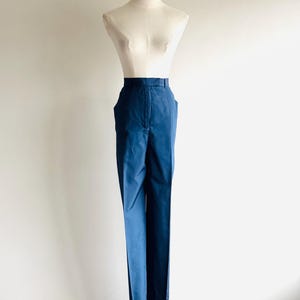 May include: A pair of navy blue trousers displayed on a mannequin. The pants have a high waist, a straight leg, and pockets. The fabric appears to be a smooth, solid color. The mannequin is set against a plain white background.