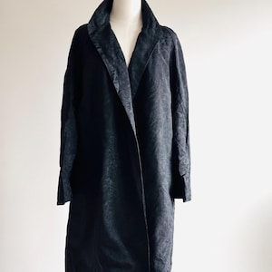 May include: A long black coat with a shawl collar. The coat is made of a textured fabric and has a relaxed fit.