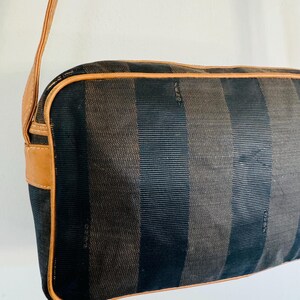 May include: A black and brown striped shoulder bag with a brown leather strap and trim. The bag has the word "FENDI" embossed on the front.