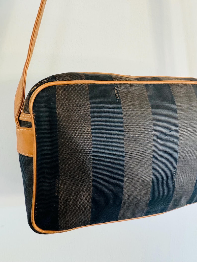 May include: A black and brown striped shoulder bag with a brown leather strap and trim. The bag has the word "FENDI" embossed on the front.