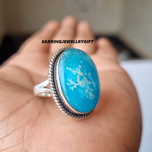 May include: A silver ring with a large oval turquoise gemstone. The gemstone has a white snowflake pattern.