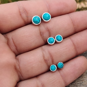 May include: A set of five turquoise gemstone earrings. The earrings are silver and have a round shape. The gemstones are a light blue colour.