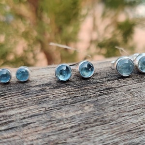 Peut inclure: Cinq paires de boucles d'oreilles en argent avec des pierres précieuses bleues. Les boucles d'oreilles sont disposées en rangée du plus grand au plus petit.