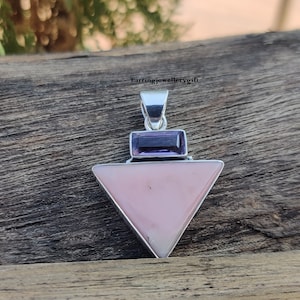 Peut inclure: Un pendentif en argent avec une opale rose en forme de triangle et une améthyste violette. Le pendentif est posé sur une surface en bois.