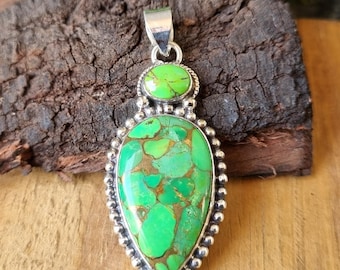 May include: A silver pendant with a teardrop-shaped green turquoise stone set in a beaded border. A smaller round green turquoise stone is set above the larger stone.
