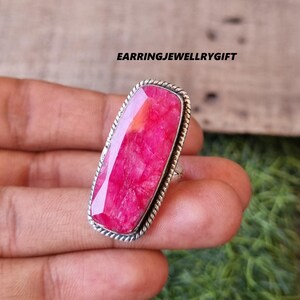 Puede incluir: Un anillo de plata con una gran piedra rectangular de rubí rosa. El anillo tiene una banda texturizada.